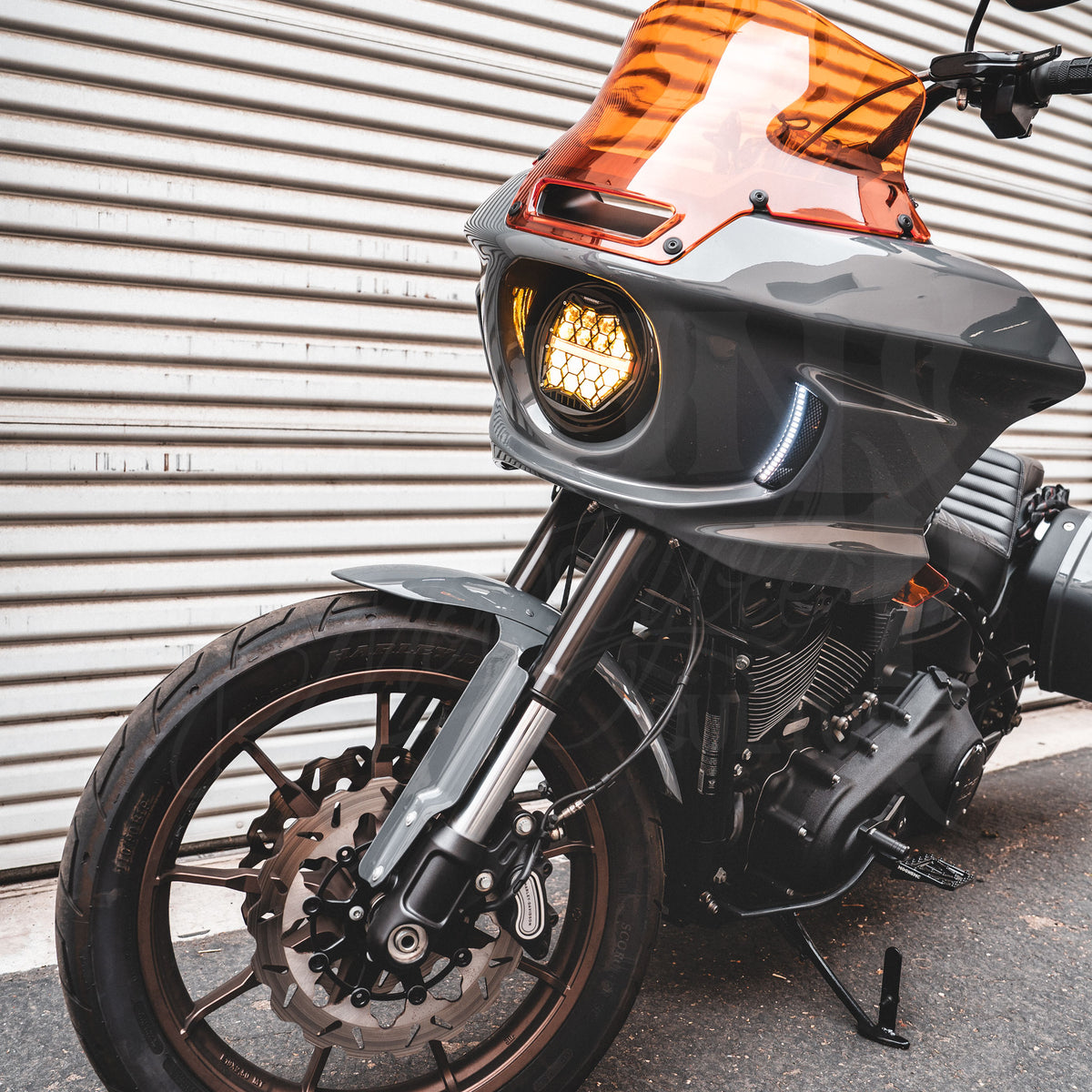 Front three-quarter view of a motorcycle with an amber HexBeam Pro headlight and orange windshield.