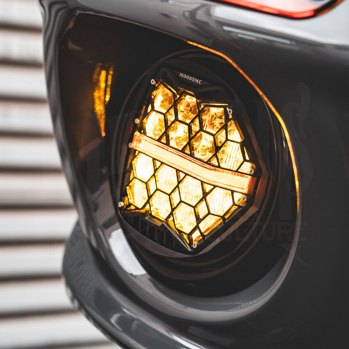 Close-up of an illuminated amber HexBeam Pro headlight mounted inside a gray motorcycle fairing.