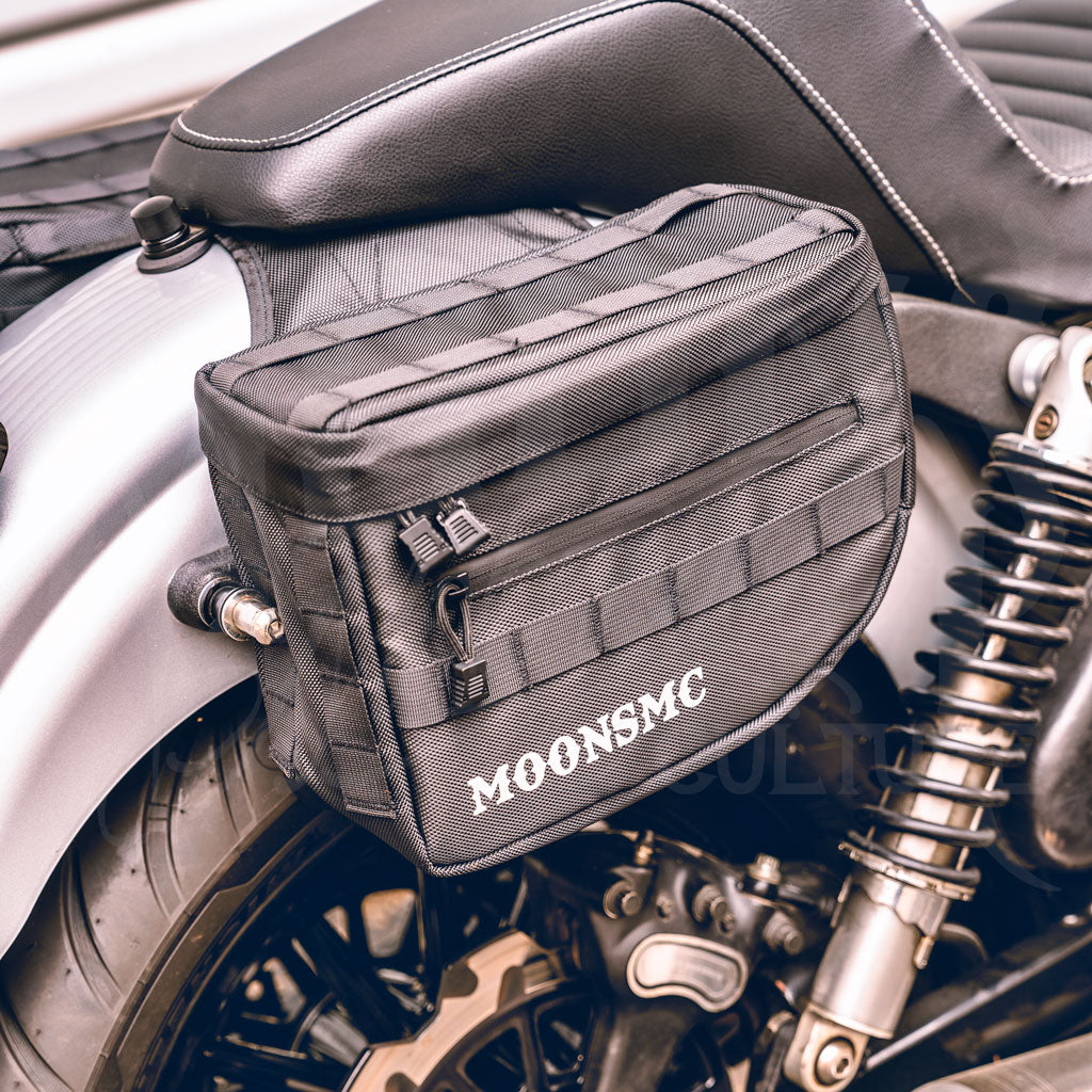 Angled front view of a MOONSMC RECON saddlebag installed beside a motorcycle seat.