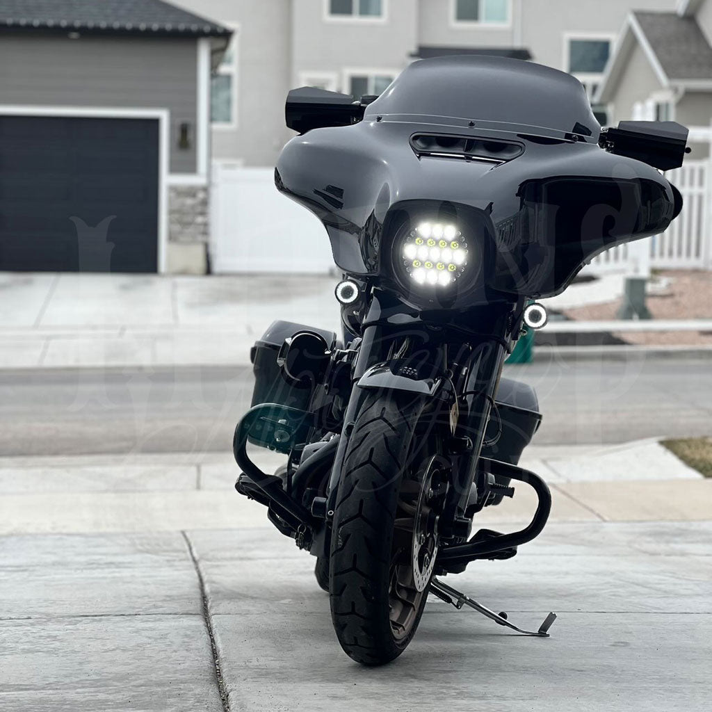 White-lit 7-inch Fly Eye V2 headlight installed in the front fairing of a black touring motorcycle.