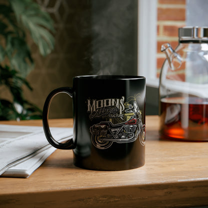 MOONSMC Red Rider FXR 11oz Black Mug: printed black mug on a wooden table beside an open book.