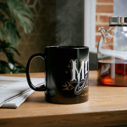 MOONSMC San Juan Capistrano Logo 11oz Black Mug: black logo mug on a wooden table beside an open book.