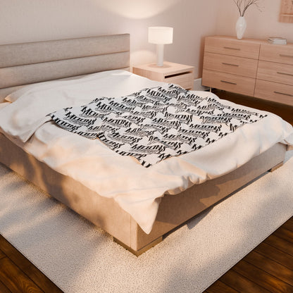 MOONSMC OG Logo plush blanket spread across a bed in a softly lit bedroom.