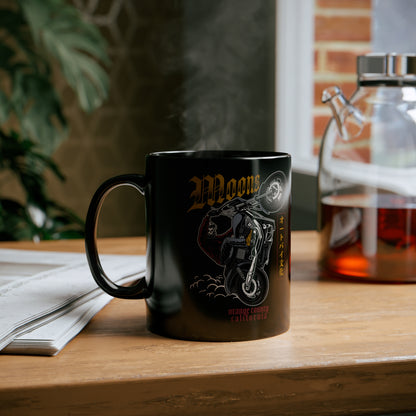MOONSMC Dyna Wheelie 11oz Black Mug: printed black mug on a wooden table beside an open book.