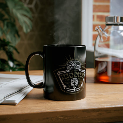 MOONSMC Skeleton - Rise of the Fly Eye 11oz Black Mug: printed black mug on a wooden table beside an open book.