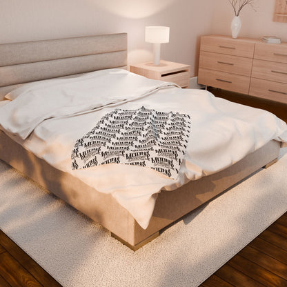 MOONSMC OG Logo plush blanket spread across a bed in a softly lit bedroom.