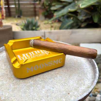 MOONSMC "The Diplomat" Cigar Ashtray: gold tray holding a cigar on an outdoor table.