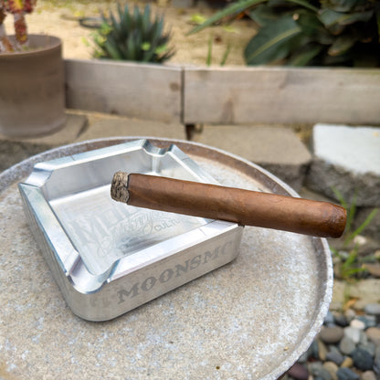 MOONSMC "The Diplomat" Cigar Ashtray: silver tray holding a cigar on an outdoor table.