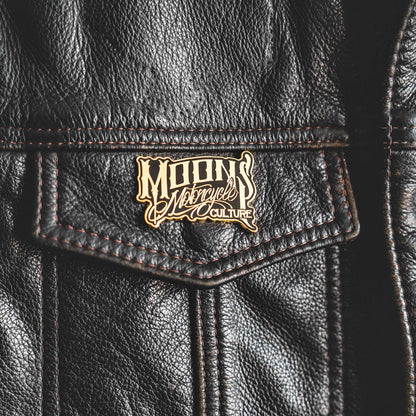 MOONSMC OG Logo Black & Gold Enamel Collector Pin: logo pin attached to a black leather vest pocket.