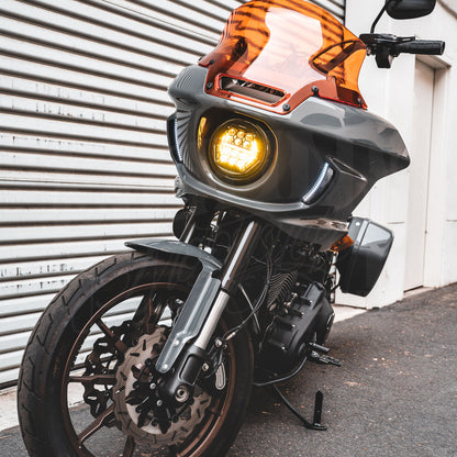 Amber HexBeam Pro headlight illuminated in a gray motorcycle fairing beneath an orange windshield.