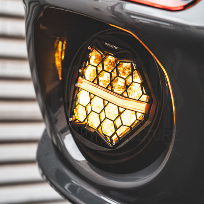Close-up of an illuminated amber HexBeam Pro headlight mounted inside a gray motorcycle fairing.