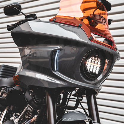 Angled view of a white-lit HexBeam Pro headlight installed beneath an orange motorcycle windshield.