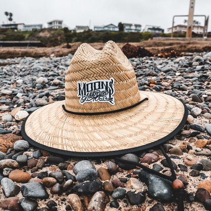 MOONSMC OG Logo UPF 50+ Lifeguard Straw Hat: straw hat resting on stones at the beach.