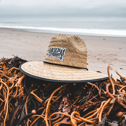 MOONSMC OG Logo UPF 50+ Lifeguard Straw Hat: straw hat resting on seaweed near the shoreline.