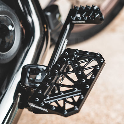 Close-up of a black MOONSMC mini floorboard installed beside a motorcycle engine.