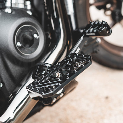 Angled view of a black MOONSMC mini floorboard installed below a motorcycle shift lever.