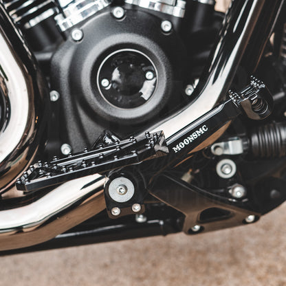 Side view of an installed MOONSMC mini floorboard showing its position beside the motorcycle engine.