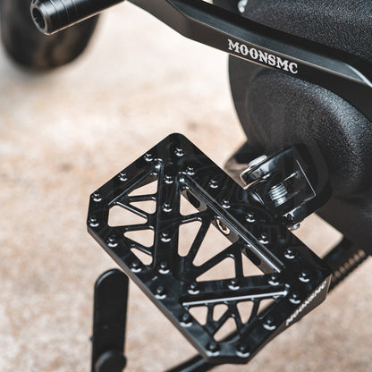 Top view of a black MOONSMC mini floorboard installed below a motorcycle engine.