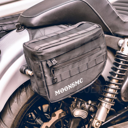 Angled front view of a MOONSMC RECON saddlebag installed beside a motorcycle seat.