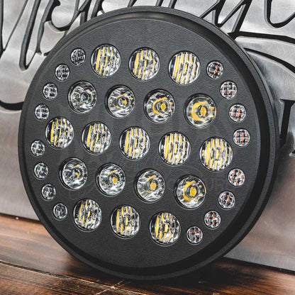 Close-up of the 7-inch Fly Eye V2 headlight and its round projector lenses resting on a wooden surface.
