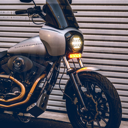 Front three-quarter view of a silver motorcycle with an amber-lit V3 LED light bar beneath its round headlight.